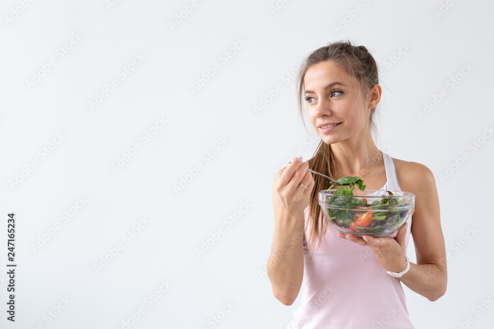 People, healthy lifestyle and fitness concept - Beautiful young woman after workout eating healthy salad on white background with copy space People, healthy lifestyle and fitness concept - Beautiful young woman after workout eating healthy salad on white background with copy space
