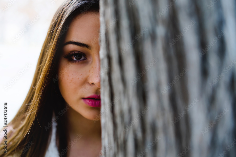 Portrait of young woman Face Behind Tree Trunk