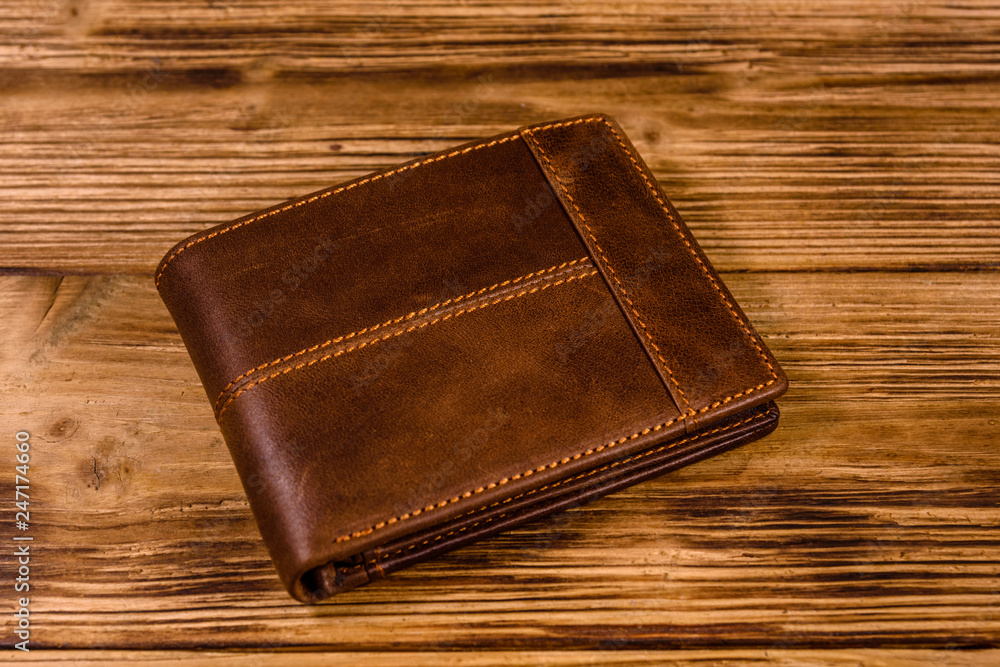 Closed brown leather wallet on wooden table Closed brown leather wallet on wooden table