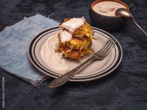 Cabbage oladi with sour cream. Against a dark background, under the plate is a blue denim napkin. photo