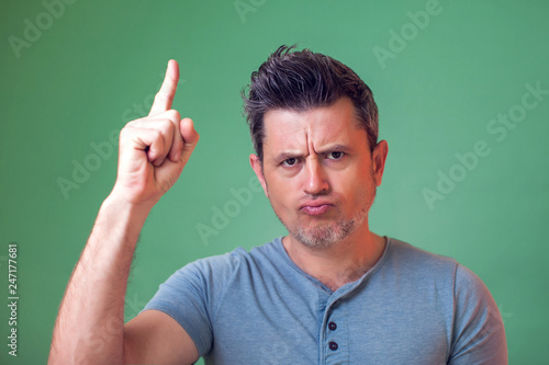 Portrait of frowing young man in casual clothes pointing fingers up. People, emotions, lifestyle concept. photo