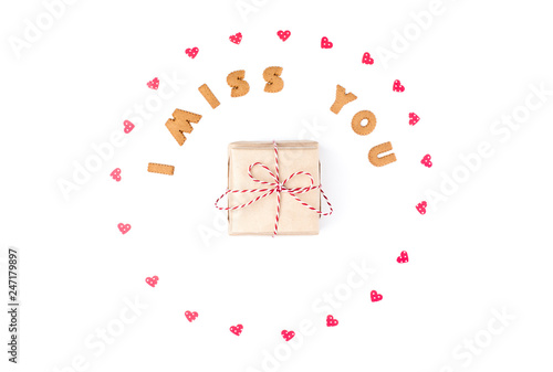 Valentine's day concept. Text I MISS YOU from cookies, frame made of paper hearts. In the center gift in craft paper. Flat lay, top view, white background, isolated, copy space