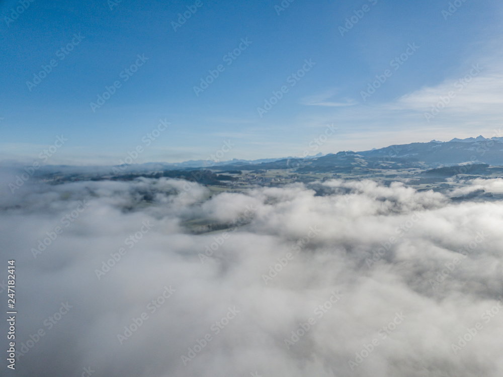 Aerial view of rural landscape in Switzerland covered with fog. Cold morning in winter with beautiful light. View from above the clouds with impressive sunlight. Aerial view of rural landscape in Switzerland covered with fog. Cold morning in winter with beautiful light. View from above the clouds with impressive sunlight.