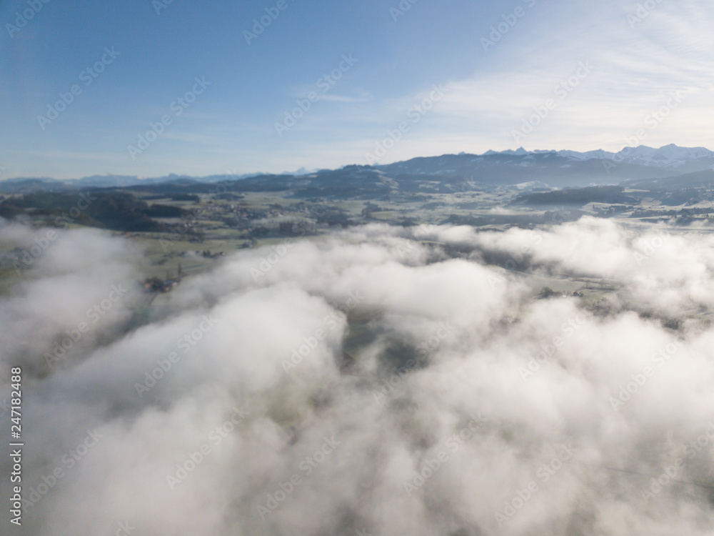 Aerial view of rural landscape in Switzerland covered with fog. Cold morning in winter with beautiful light. View from above the clouds with impressive sunlight.
