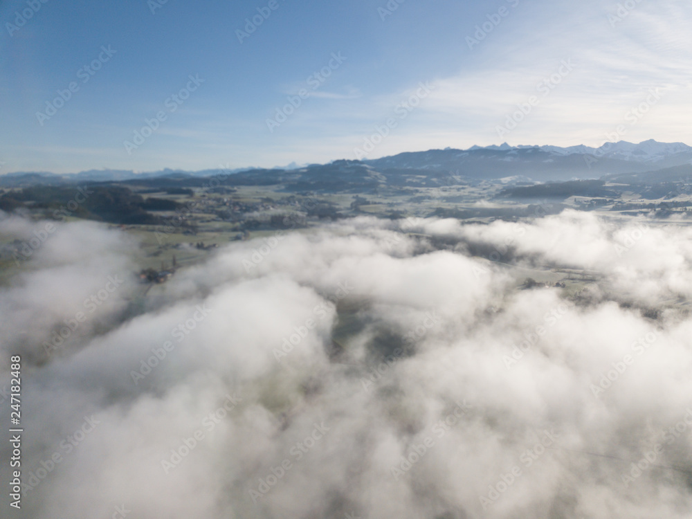 Aerial view of rural landscape in Switzerland covered with fog. Cold morning in winter with beautiful light. View from above the clouds with impressive sunlight. Aerial view of rural landscape in Switzerland covered with fog. Cold morning in winter with beautiful light. View from above the clouds with impressive sunlight.