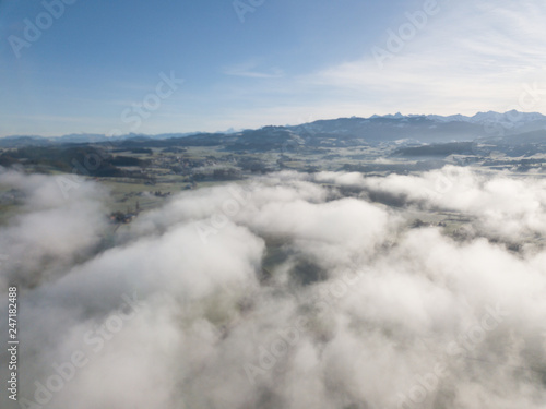 Aerial view of rural landscape in Switzerland covered with fog. Cold morning in winter with beautiful light. View from above the clouds with impressive sunlight.