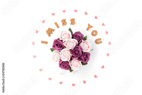 Valentine's day concept. Text I MISS YOU from cookies, frame made of paper hearts. In the center flowers in a box. Flat lay, top view, white background, isolated, copy space