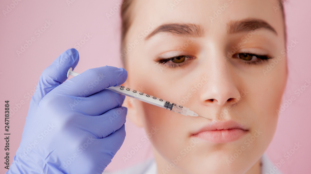 Doctor in gloves giving woman botox injections in lips, on pink background Doctor in gloves giving woman botox injections in lips, on pink background