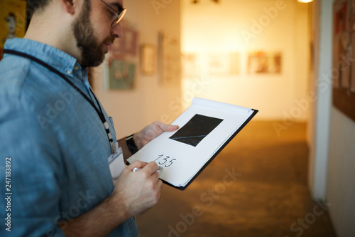 Portrait of unrecognizable man holding clipboard taking notes on pictures in art gallery, copy space