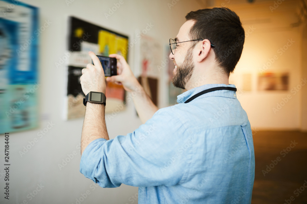 Fototapeta premium Side view portrait of smiling man taking smartphone photo of painting in art gallery, copy space