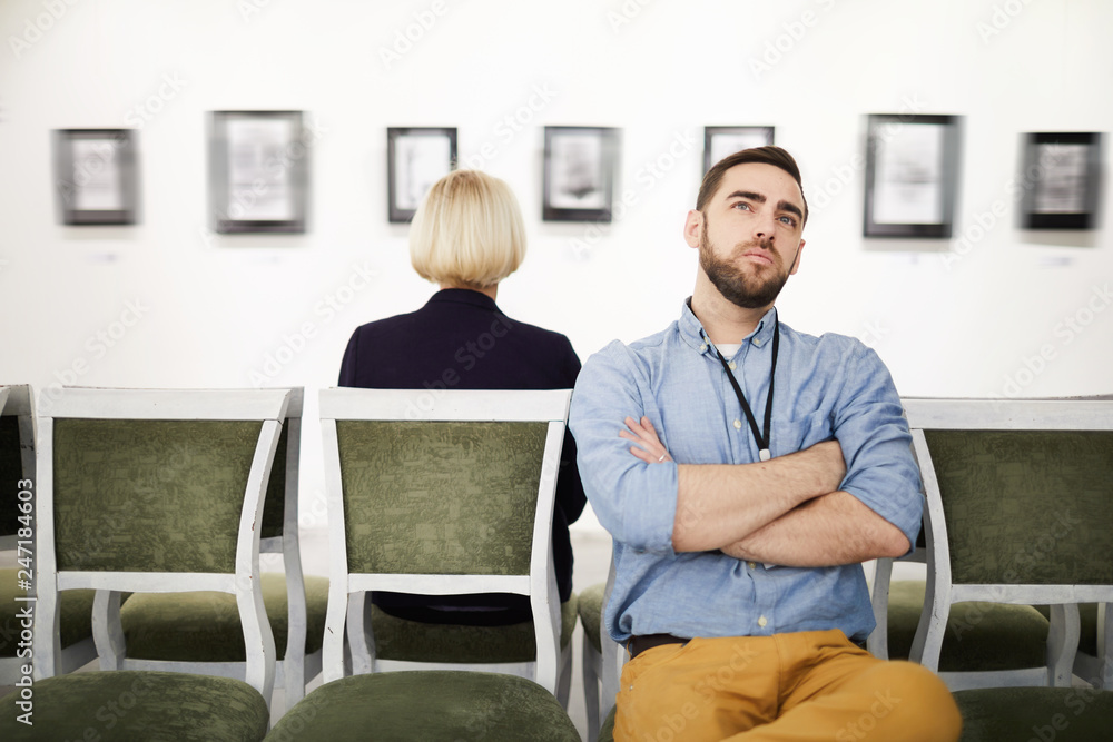 Portrait of bearded young man looking at pictures in art gallery or museum while sitting on velvet chair, copy space Portrait of bearded young man looking at pictures in art gallery or museum while sitting on velvet chair, copy space