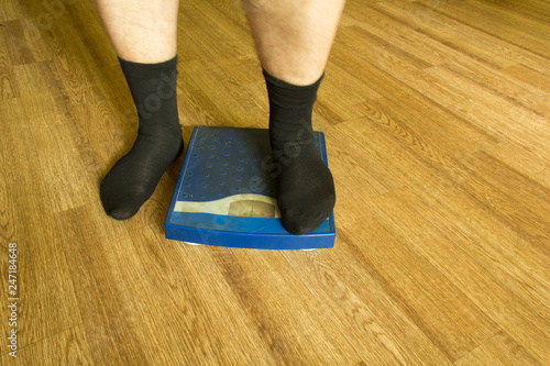 Men's legs in black socks stand on a mechanical scales of blue color (front view)