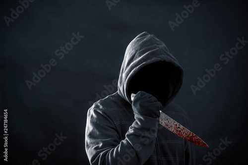 Hooded man with bloody knife in the dark 
