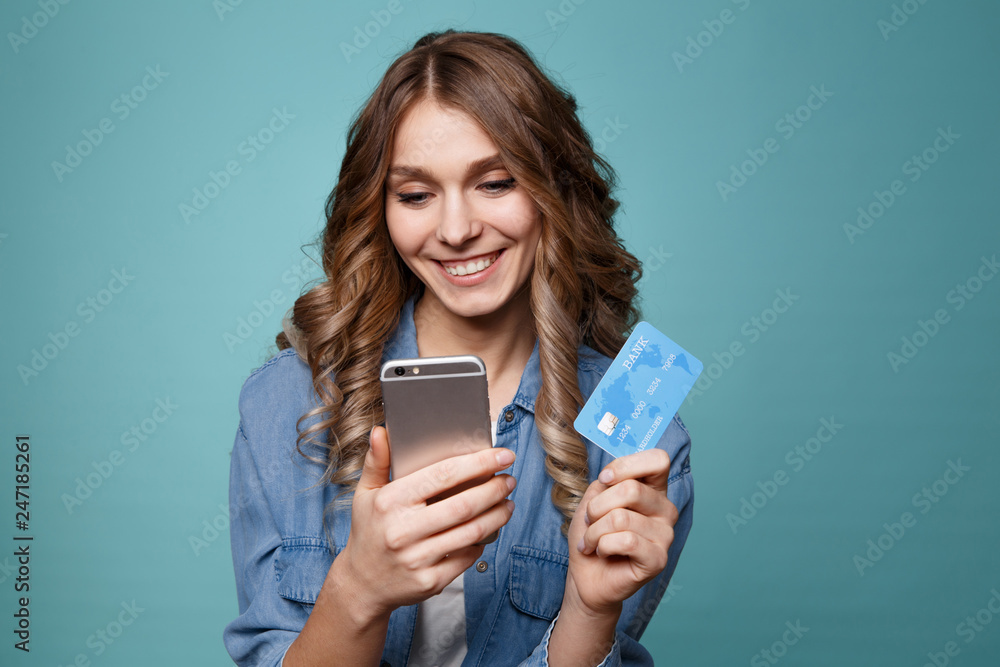Image of excited young lady isolated over blue background using mobile phone holding credit card. Image of excited young lady isolated over blue background using mobile phone holding credit card.