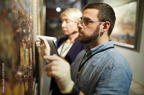 Waist up portrait of two museum workers inspecting painting for restoration, copy space photo