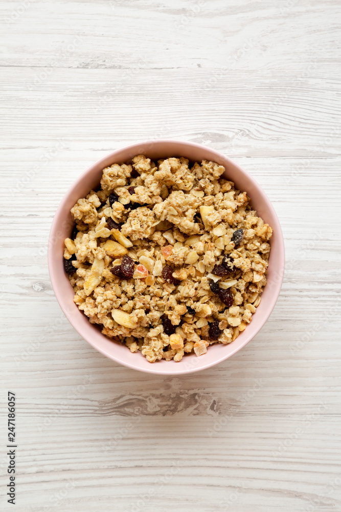 Fruit granola in pink bowl over white wooden background, top view. Flat lay, from above, overhead. Fruit granola in pink bowl over white wooden background, top view. Flat lay, from above, overhead.