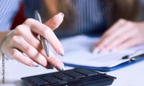 Business woman hand using a calculator with silver pen in office closeup.