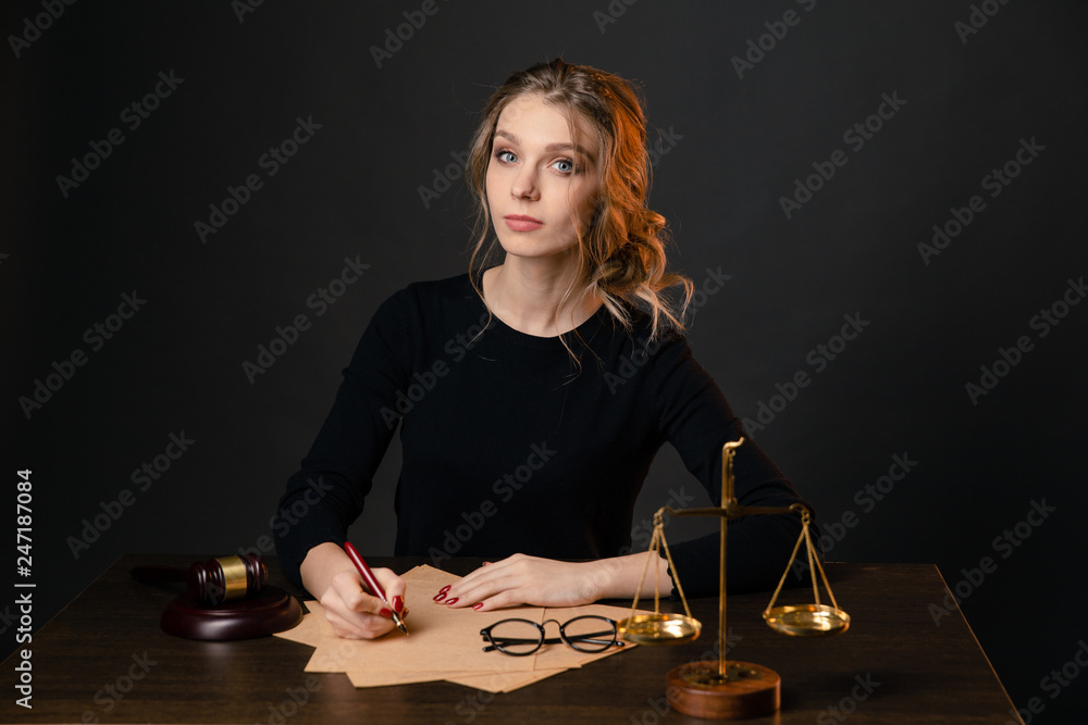 Young lawyer woman in a formal dress sitting at table and writing something by pen, lawyer woman with bright red nails working isolated over the black backgrownd Young lawyer woman in a formal dress sitting at table and writing something by pen, lawyer woman with bright red nails working isolated over the black backgrownd