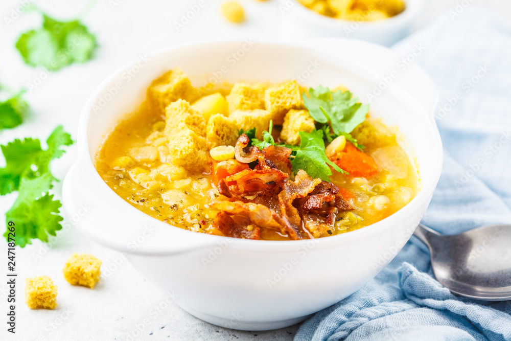 Split pea soup with smoked bacon and crackers in white plate.