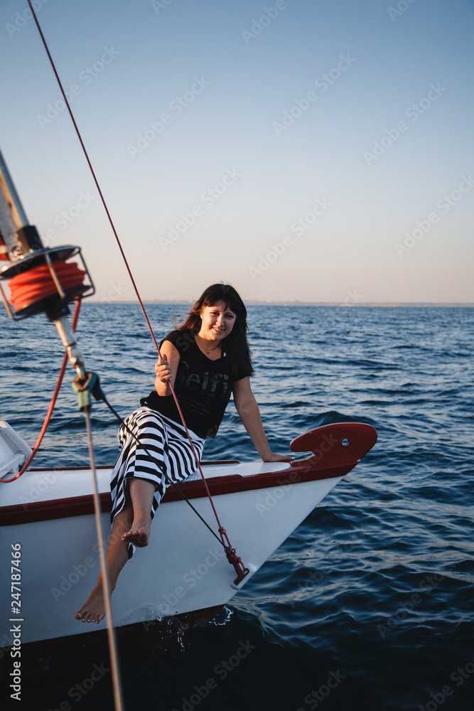 Obraz premium Young pretty woman in black shirt and striped skirt at luxury yacht in sea, sunset