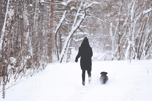 Teenager boy with a black labrador retriever in the winter forest.