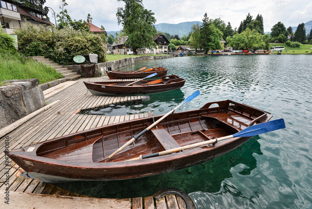 Obraz premium Beautiful Lake Bled in the Julian Alps and two old wooden boats. Mountains, clear aquamarine water, tourist boat, lake and dramatic blue sky.
