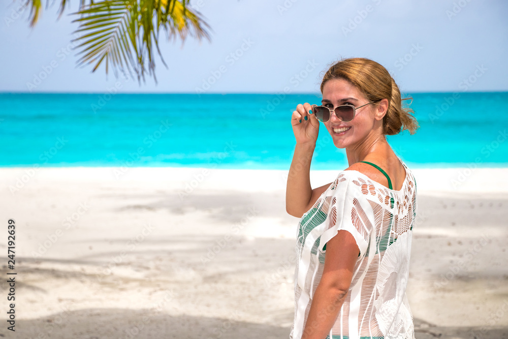 Young woman with sunglasses at the dream beach laughs at the camera Young woman with sunglasses at the dream beach laughs at the camera