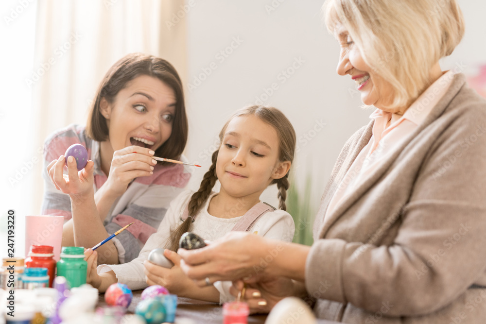 Playful young woman pointing at her daughter with paintbrush while having fun and painting eggs for Easter Playful young woman pointing at her daughter with paintbrush while having fun and painting eggs for Easter