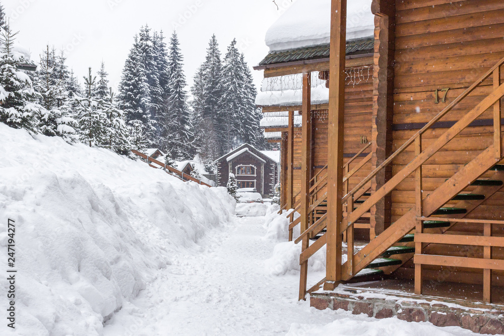Fototapeta premium Chalet in the ski resort. Wooden house in the resort Bukovel in Ukraine. Two-storey cottages of logs. Natural building materials. Winter country landscape. Snow-covered houses. Wooden facade.