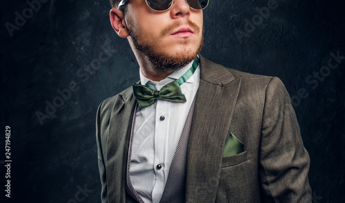 A stylish man in sunglasses dressed in an elegant suit against a dark textured wall