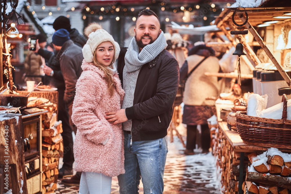 A happy attractive couple wearing warm clothes standing together near a shop counter of a winter fair at a Christmas time.