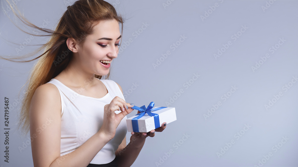 happy woman opening gift box on a studio background, the girl untying blue ribbon bow and wondering, concept holidays and miracles happy woman opening gift box on a studio background, the girl untying blue ribbon bow and wondering, concept holidays and miracles