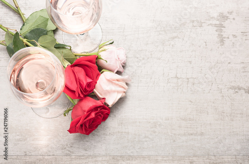 Top down view of two glasses of rosé wine with red and pink roses on a reclaimed wood background.