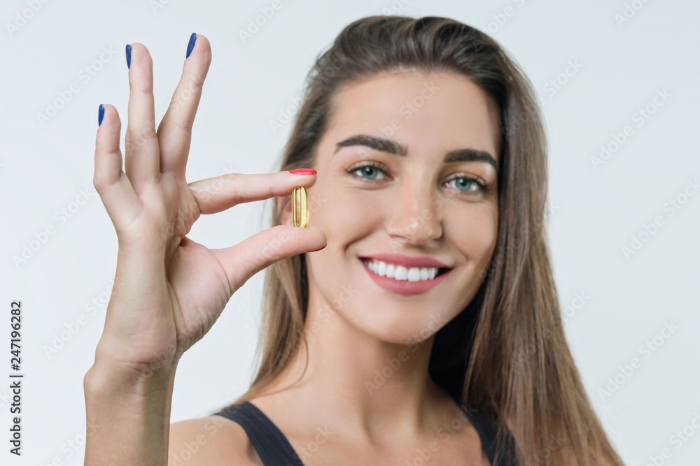 Obraz premium Young smiling beautiful healthy woman in sportswear with vitamin D, E, A fish oil omega-3 capsules, on white background