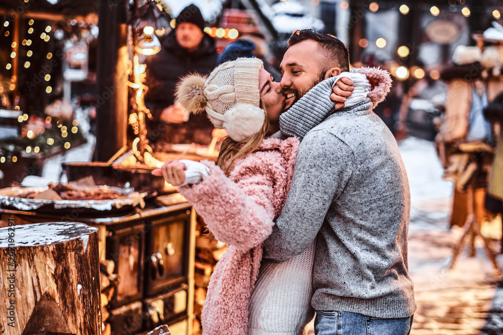 A cheerful attractive couple in love, enjoying spending time together while embracing at the winter fair at a Christmas time A cheerful attractive couple in love, enjoying spending time together while embracing at the winter fair at a Christmas time