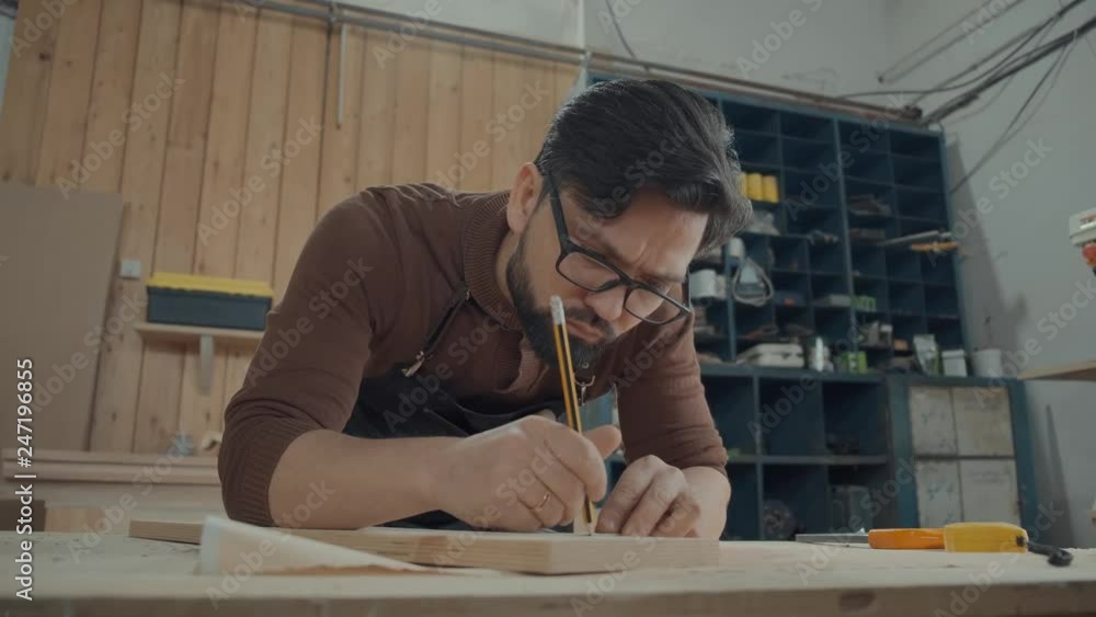 Man in carpentry workshop leaned over a table with tools, made notes ...