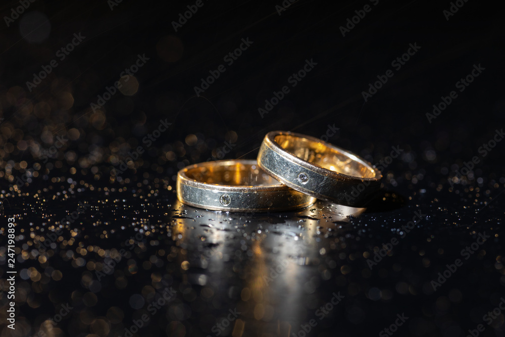 Wedding rings lying on dark surface shining with light close up macro. Water splashes Wedding rings lying on dark surface shining with light close up macro. Water splashes