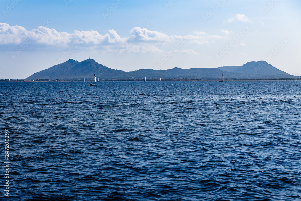wide, blue sea waters on a sunny day, yachts with white sails in the distance and mountains on the horizon