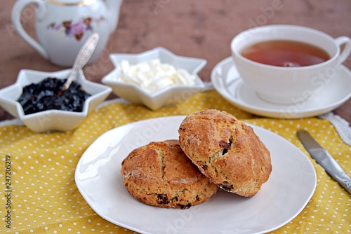 Traditional English scones with dried cranberries on a white plate. Served with jam and whipped cream.