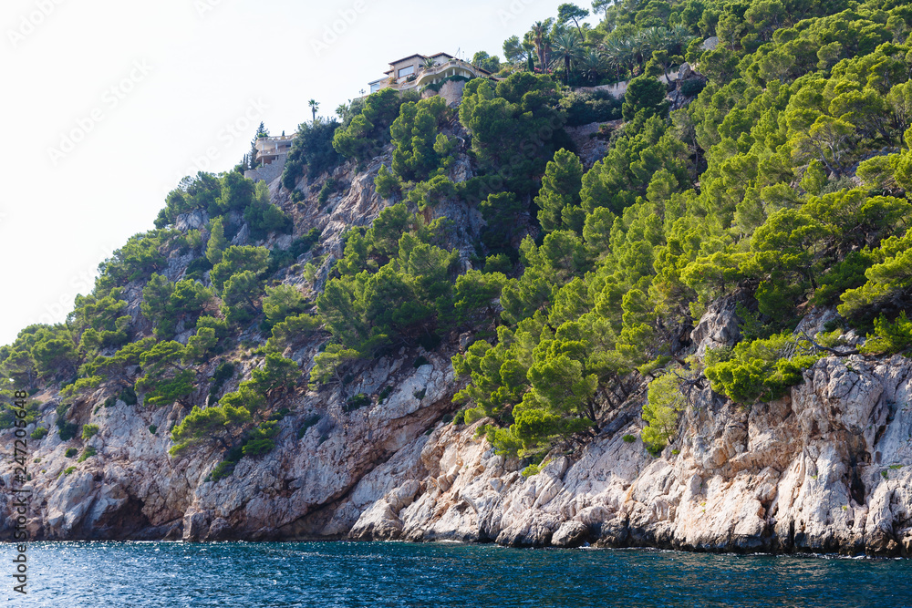 sunny summer day at sea, view from yacht to rocky shore trees and buildings on steep bank