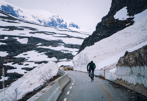 Fototapeta Cyclist on mountain road in Norway, cycling uphill on way after snow avalanche