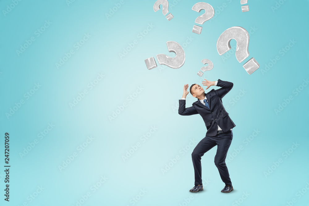 Grey question marks falling on a businessman on blue background Grey question marks falling on a businessman on blue background