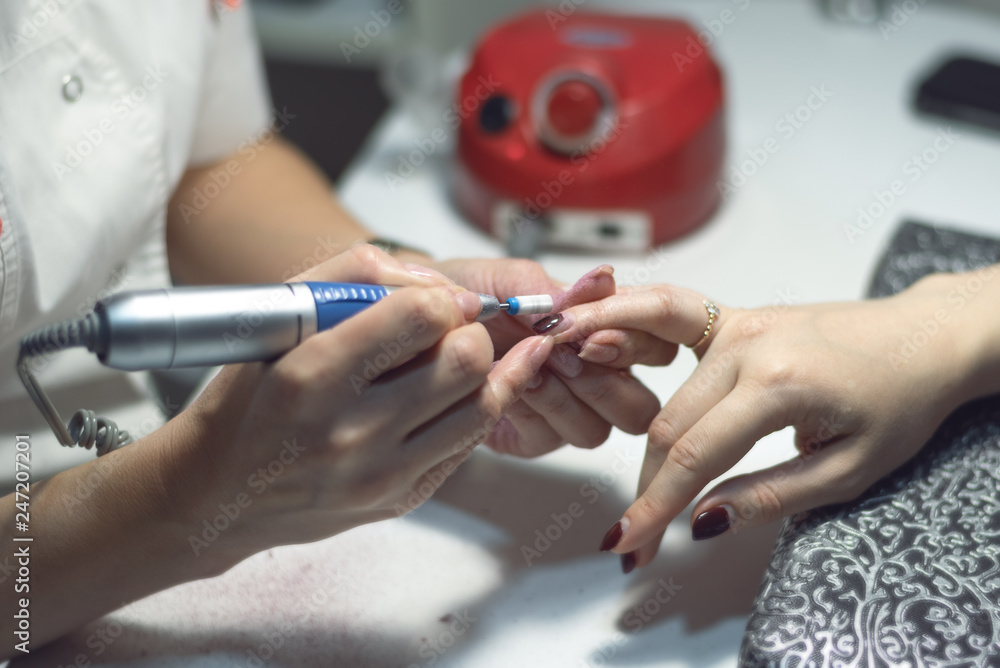 Manicurist master is removing an old nail varnish by hardware manicure. Nail care concept. Manicurist master is removing an old nail varnish by hardware manicure. Nail care concept.