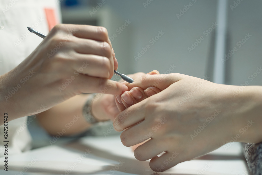 Manicurist is using a nail scraper on the female fingernails. Nail care concept. Manicurist is using a nail scraper on the female fingernails. Nail care concept.