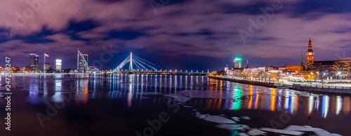 Panoramic Cityscape of Riga, Latvia from Akmens Bridge at Night with Dramatic Sky, with the View of Office Buildings and other Bridges over River Daugava