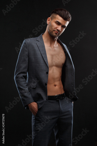 Young sexy man in a jacket over his naked body against a dark background.