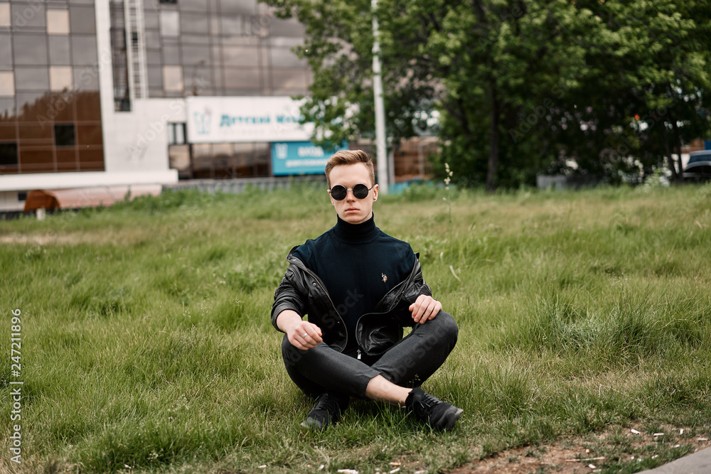 Fototapeta premium man in the hat wears sunglasses sitting on the grass
