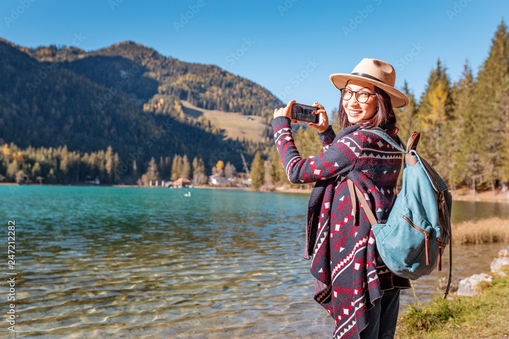 Happy young traveler woman having fun on a coast of a Dobbiaco lake in Dolomites Alps, Italy