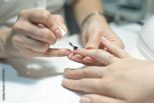 Manicurist is applying a nail base gel on a female finger nails. Nail care concept.