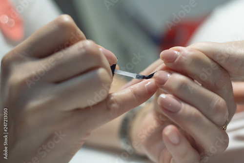 Manicurist is applying a nail base gel on a female finger nails. Nail care concept.